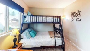 Een slaapkamer met een stapelbed, raam, decoratie aan de wand en een bedlampje.