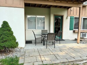 Eine Terrasse im Freien mit Tisch und Stühlen, eine Tür mit Fenster und ein kleiner Baum.