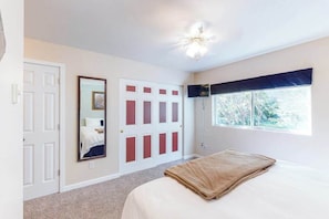 Een slaapkamer met een bed, een groot raam, een plafondventilator en een deur met een spiegel.