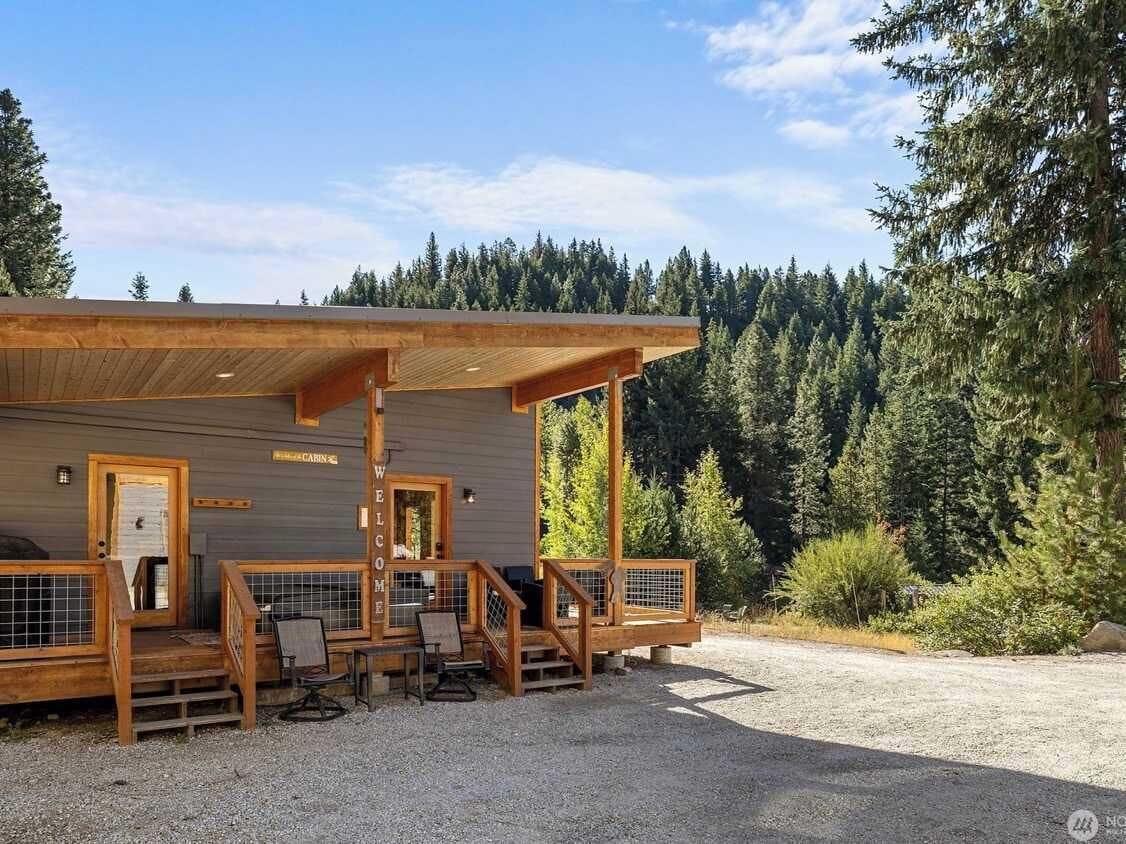 A cabin with a wooden porch, a welcome sign, and a gravel driveway.