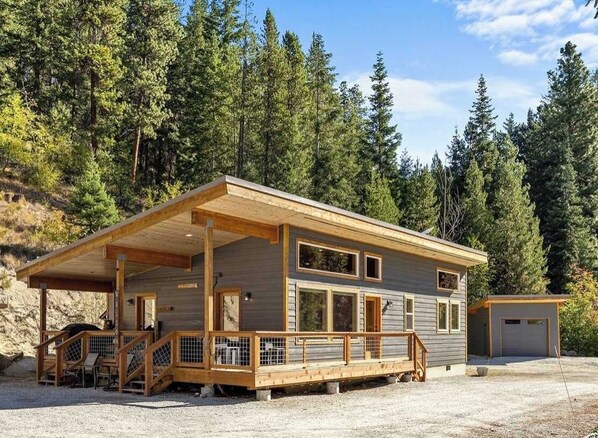 A cabin with a covered porch, a garage, and a view of a forested area. - Woodland 3BR Mountainview Dog Friendly - Hot Tub (Leavenworth)