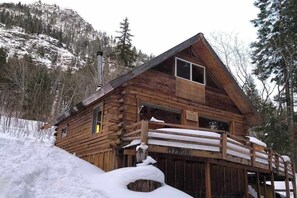 Eine Holzhütte mit steilem Dach, umgeben von verschneitem Gelände und Bäumen.
