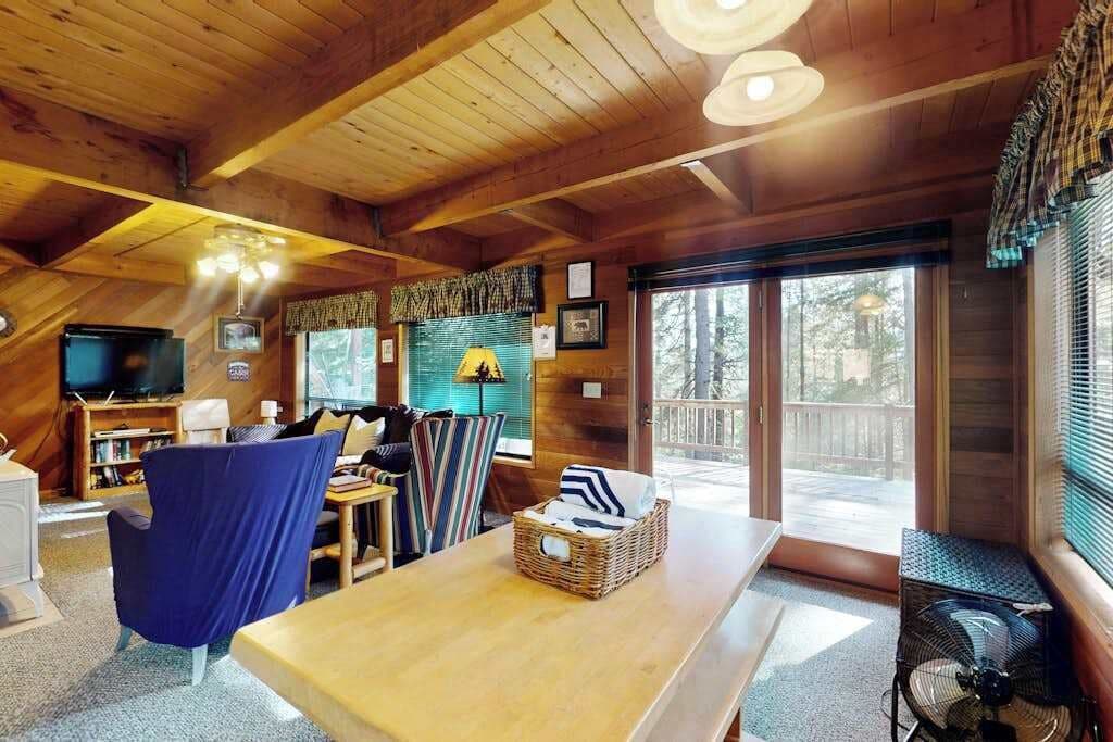 Een gezellig cabin interieur met een houten plafond, een eethoek, een televisie en een groot raam.
