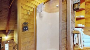 Puinen sisustus, jossa on suihku, pyyhekoukku ja pieni hylly, jossa on hygieniatuotteita.