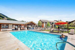 A swimming pool with lounge chairs and umbrellas, surrounded by buildings with wooden facades.
