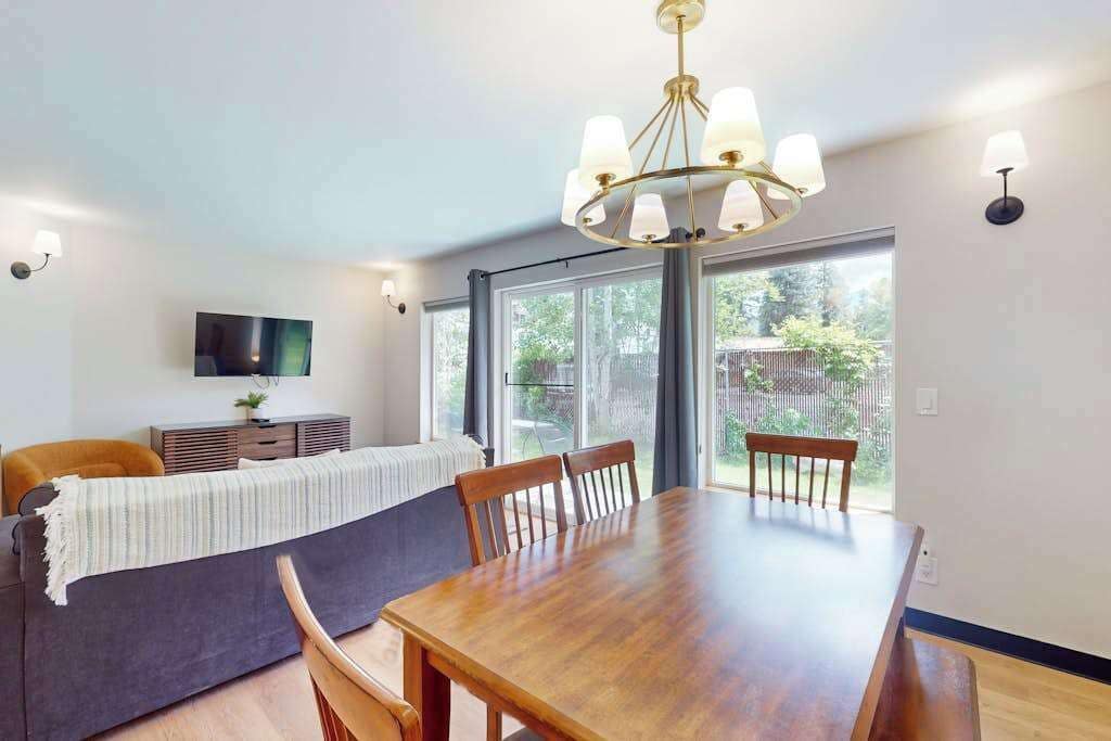 A dining area with a wooden table and chairs, a chandelier, and a television on a cabinet.