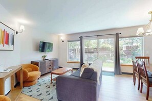 A modern living room with a sofa, a coffee table, a TV, and a dining area with chairs and a table.
