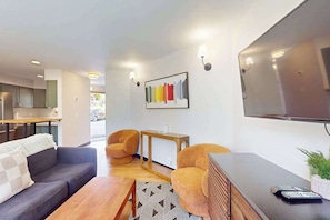 Ein modernes Wohnzimmer mit einer Couch, Sesseln, einem Couchtisch, einem Fernseher und einem Wandbild.