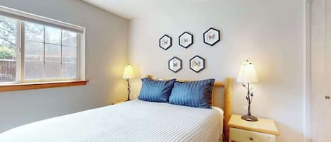 A bedroom with a bed, two bedside tables, a window, and wall art.