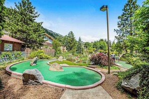 Un campo de mini golf con una superficie de césped verde, rodeado de árboles y un edificio de madera.
