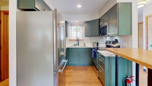 A modern kitchen with a stainless steel refrigerator, teal cabinetry, and a wooden countertop.