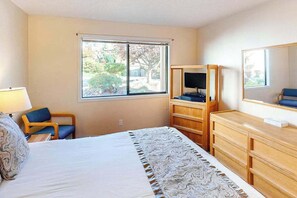 A hotel room with a bed, a desk, a chair, a dresser, a television, and a window with a view of trees. - 1BR lakefront condo near beach with pool & hot tub (Chelan)