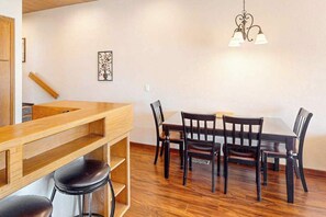 A dining area with a wooden table and chairs, a bar counter with stools, and a hanging light fixture.