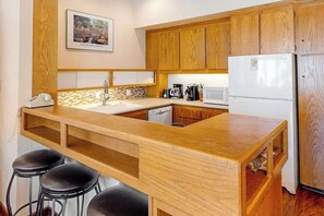 Eine Küche mit Holzschränken, einem weißen Kühlschrank, einer Kaffeemaschine und einem Spülbecken.
