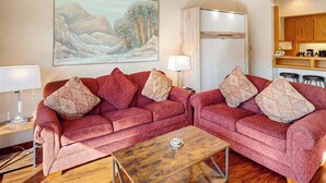 A living room with two red sofas, a coffee table, and a painting on the wall. - 1BR lakefront condo near beach with pool & hot tub (Chelan)