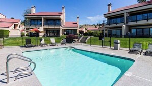 A swimming pool with a metal ladder, surrounded by lounge chairs and umbrellas, with buildings in the background. - 1BR lakefront condo near beach with pool & hot tub (Chelan)