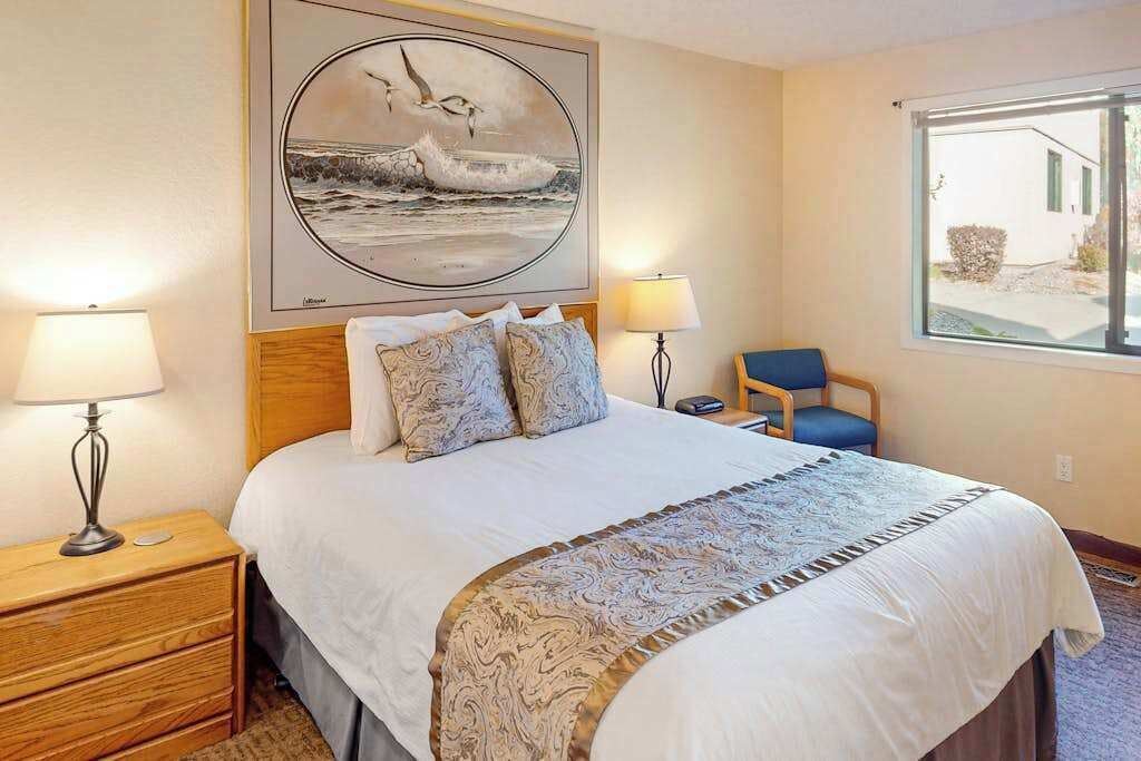A hotel room with a bed, two bedside lamps, a chair, a window, and a painting on the wall.