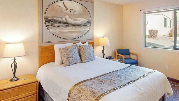 A hotel room with a bed, two bedside lamps, a chair, a window, and a painting on the wall. - 1BR lakefront condo near beach with pool & hot tub (Chelan)