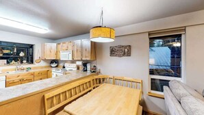 A modern kitchen with wooden cabinets, a central island, and a dining area with a bench. - Woodland 2BR Mountainview Dog Friendly - Deck (Leavenworth)