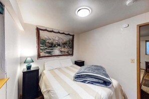 A bedroom with a bed, a nightstand, a lamp, and a painting on the wall. - Woodland 2BR Mountainview Dog Friendly - Deck (Leavenworth)