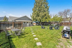 A backyard with a dining table, chairs, a grill, and a large tree. - 3BR Lakeview Dog Friendly - Patio - W&D (Manson)