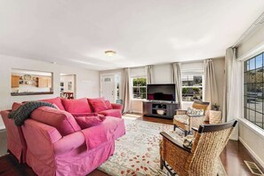 A living room with a pink sofa, a flat-screen TV, wicker chairs, and a large window. - 3BR Lakeview Dog Friendly - Patio - W&D (Manson)