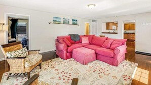 Uma sala de estar com um sofá seccional rosa, uma poltrona de vime e um tapete estampado.