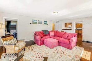 A living room with a pink sectional sofa, a wicker armchair, and a patterned rug. - 3BR Lakeview Dog Friendly - Patio - W&D (Manson)