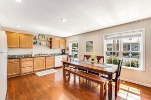 A kitchen with wooden cabinets, a dining table, and a view through large windows.