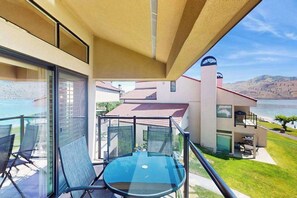 Ein Balkon mit Glastisch und Stühlen, der auf ein Gewässer und ein Gebäude mit rotem Dach blickt.