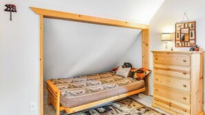 Un dormitorio pequeño con una cama individual, un aparador de madera y un techo inclinado.