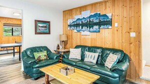 Una sala de estar acogedora con un sofá de cuero verde, una mesa de centro de madera y un cuadro colgado en la pared que representa un paisaje montañoso.