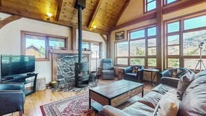 A cozy living room with a stone fireplace, comfortable seating, and large windows offering a view of the outdoors. - Unique 2BR Lakefront - Hot Tub - Dock - Deck (Chelan)