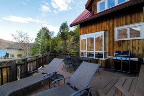 Eine Holzterrasse mit Liegestühlen und einem Grill mit Blick auf eine gebirgige Landschaft.