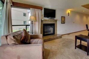 Ein Wohnzimmer mit einer Couch, einem Fernseher über einem Kamin und Blick auf ein Gebäude.