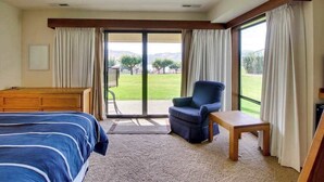 A hotel room with a bed, a chair, a small table, and a view of a grassy area through a sliding door. - 2BR Lakefront - Pool - Tennis - Hot Tub - Balcony (Chelan)