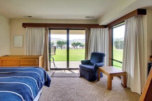 Ein Hotelzimmer mit einem Bett, einem Sessel, einem kleinen Tisch und Blick auf eine Rasenfläche durch eine Schiebetür.