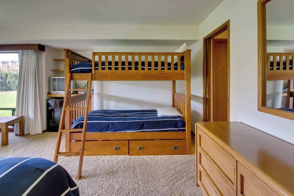 A bunk bed with a desk and chair, a dresser, and a window with curtains.