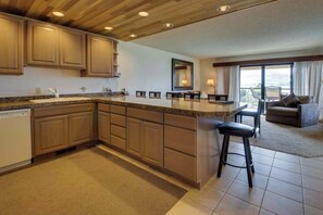 A kitchen with wooden cabinets, a granite countertop, and a bar area with stools. - 2BR Lakefront - Pool - Tennis - Hot Tub - Balcony (Chelan)