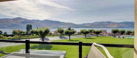 A balcony with a view of a lake and mountains, a table, and chairs.