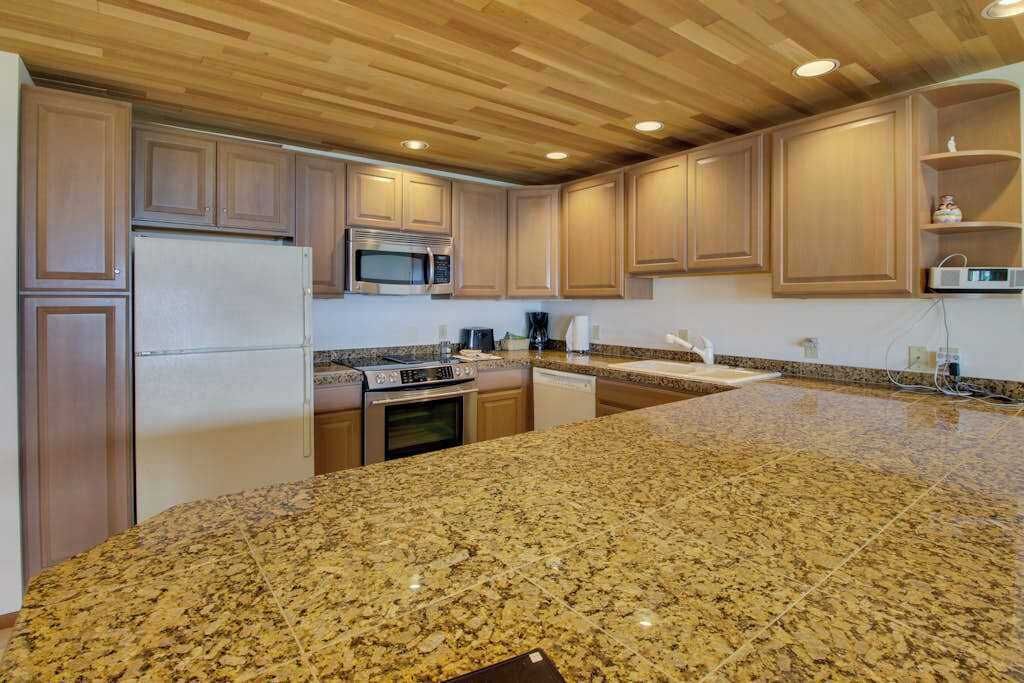 Eine Küche mit Granit Arbeitsplatten, Holzschränken, einer Mikrowelle, einem Kühlschrank und einem Geschirrspüler.