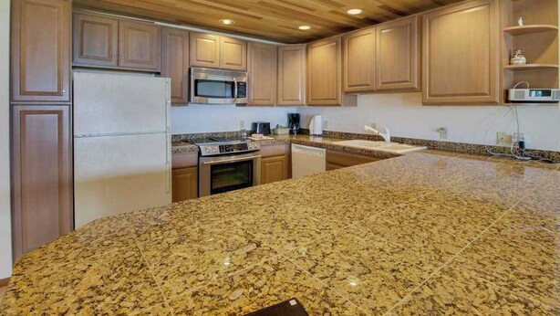 A kitchen with granite countertops, wooden cabinets, a microwave, a refrigerator, and a dishwasher. - 2BR Lakefront - Pool - Tennis - Hot Tub - Balcony (Chelan)