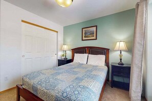 Een slaapkamer met een bed, twee nachtkastjes, een deur en een aan de muur hangend schilderij.