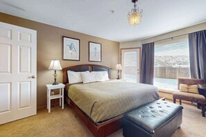 Ein Schlafzimmer mit einem Bett, Nachttischen, einer Bank, einer Chandelüster und einem Fenster mit Vorhängen.