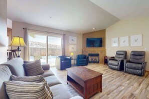 Ein Wohnzimmer mit einer Couch, Sesseln, einem Couchtisch, einem Kamin und einem Fernseher.