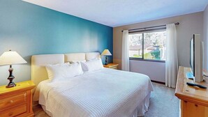 Ein Hotelzimmer mit einem Bett, Nachttischlampen, einem Schreibtisch mit Computer und einem fenster mit Vorhängen.