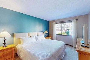 Ein Hotelzimmer mit einem Bett, Nachttischlampen, einem Schreibtisch mit Computer und einem fenster mit Vorhängen.