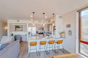 A modern kitchen with bar stools, a dining area with a table, and a large window with a view. - 2BR Mountainview 2nd-Floor - Balcony - Pool (Chelan)
