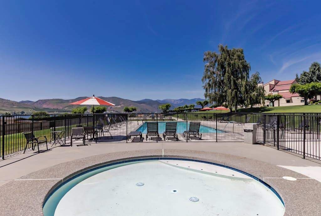 Una piscina con vista a las montañas, un patio cercado con sillas y un edificio de techo rojo.