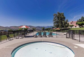 A swimming pool with a view of mountains, a fenced patio area with chairs, and a building with a red roof. - 1BR Lakeview 2nd-Floor - Balcony - Pool (Chelan)
